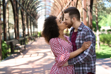 Fototapeta premium Young loving interracial couple kissing in park on spring day