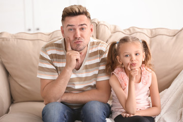 Funny father and daughter sitting on sofa at home