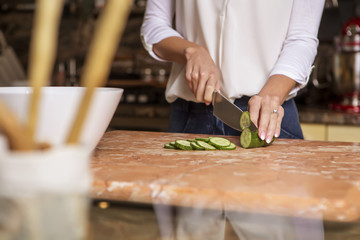 Beautiful young brunette woman in casual outfit cooking in the kitchen in her home. Luxury rich interior