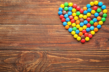 Heart made of colorful candies on wooden background