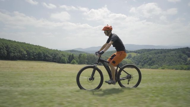 4K footage, man on electric mountain bike cycling on meadow in hilly landscape on cloudy summer day
