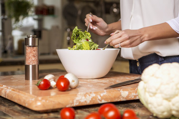 Beautiful young brunette woman in casual outfit cooking in the kitchen in her home. Luxury rich interior