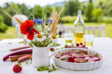 Baked rhubarb and fresh strawberries on a wooden table in the garden. 