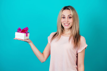 cheerful attractive woman smiling and holding a box with a gift on a blue background in the studio.