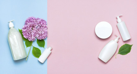 Cosmetic bottle containers with hydrangea flower on a blue and pink minimalistic background flat lay. Blank label for branding mock-up. Natural beauty product concept.