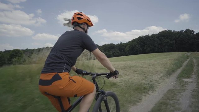 4k sport footage, man on e mountainbike cycling up path between meadows
