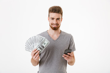 Man standing isolated using mobile phone holding money. Looking camera.