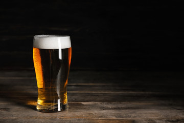 Glasses with cold beer on wooden table against dark background