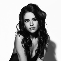 Naklejka premium Young sexy slim tanned woman in black swimsuit posing against white background. Black and white fashion portrait of beautiful girl with long wavy brunette hair. Swimwear or bikini model.