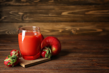 Glass of tasty smoothie, apples and strawberries on wooden background