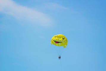 Big yellow fun parachute with painted mug carries people through air against blue sky