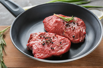 Frying pan with raw meat, herbs and spices on wooden board