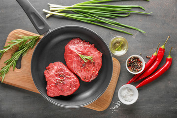 Frying pan with raw meat, herbs and spices on wooden board