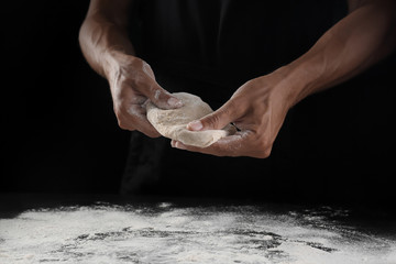 Fototapeta na wymiar Man kneading dough on black background