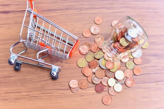 Top View of Mini Shopping Cart or Trolley and Glass Jar with Coins Spilling Out