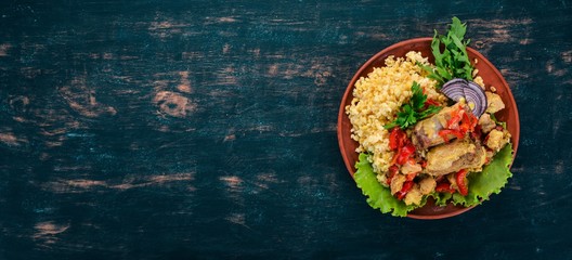 Bulgur with meat, paprika, cherry tomatoes, and vegetables. On a wooden background. Top view. Copy space.