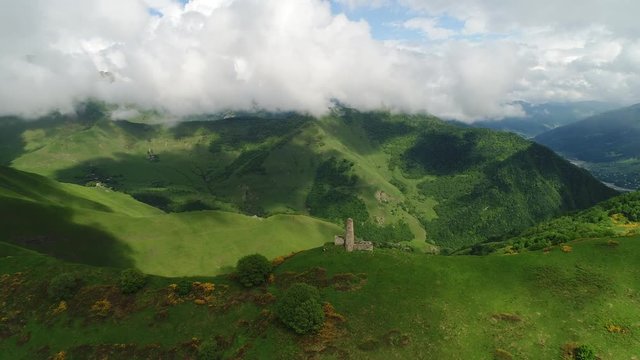 Flying over olden Caucasian  traditional fortress tower on high green hill in picturesque mountain scenery. Breathtaking view. Aerial view.