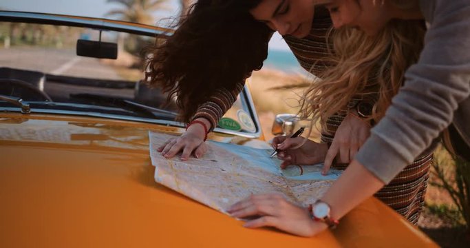 Young women on road trip with convertible car reading map