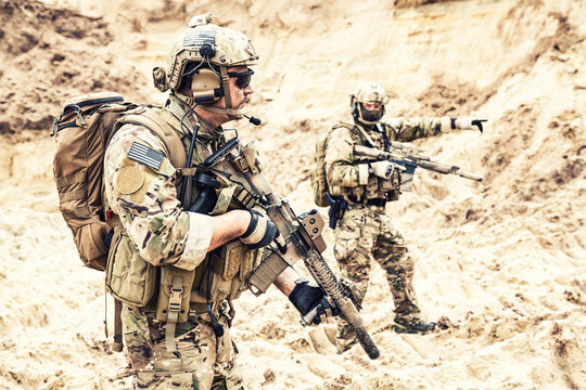 Two armed US army commandos or military scouts equipped with radio headset moving forward in sands during enemy area reconnaissance. Special forces operation, long range surveillance mission in desert