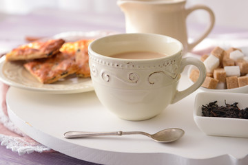Cup of aromatic tea with milk and sweets on table