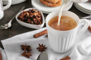 Adding milk to delicious tea on table
