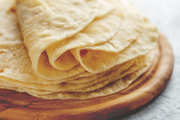 Stack of homemade wheat flour tortilla wraps on wooden cutting board. - 210154328