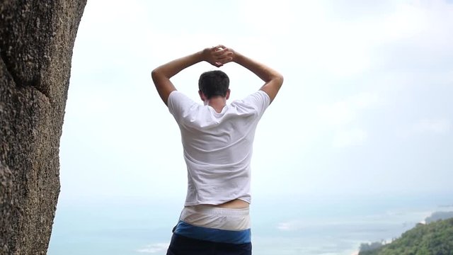 A tourist man stands on the edge of the mountain with a beautiful scenery, raised his hands up, feels freedom and wind. slow motion, 1920x1080, full hd