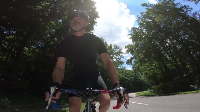 4K sport video man cycling out of saddle on race bike on curvy asphalt road through summer 

