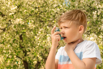 Little boy using inhaler near blooming tree. Allergy concept