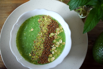 Green smoothie bowl topped with nuts, flax seeds and oatmeal flakes