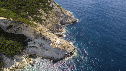 Aerial view of a rocky coastline overlooking the Mediterranean Sea. On the mountain grows a forest with many trees and there is some big rock in the blue and azure sea.