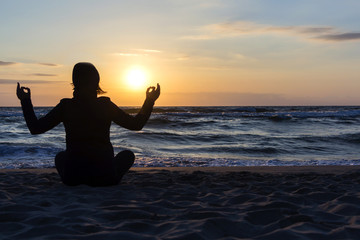silhouette of Young woman sitting back, meditate in lotus yoga pose outdoor, on the beach.