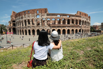 Due amiche abbracciate e sedute sull'erba guardano il Colosseo in una bellissima e soleggiata giornata a Roma, Italia