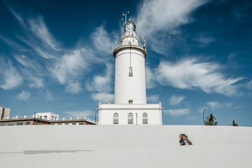 White lighthouse with blue sky background, and people walking in the street.
