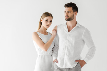 attractive woman in linen white dress embracing boyfriend with hands in pockets isolated on grey background