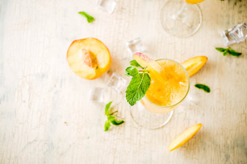 Summer cold alcohol beverage, iced peach Bellini cocktail with mint leaves, light concrete background copy space