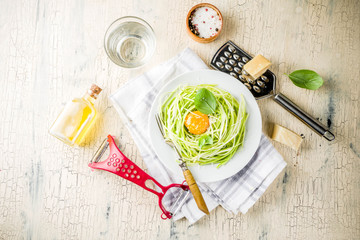 Trendy vegan food recipes, cheese zucchini spaghetti pasta with egg yolk with parmesan, olive oil and basil leaves, light concrete background copy space