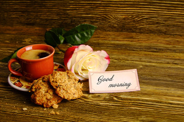 A cup of coffee, biscuits and a rose on a wooden background
