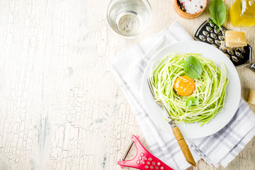 Trendy vegan food recipes, cheese zucchini spaghetti pasta with egg yolk with parmesan, olive oil and basil leaves, light concrete background copy space