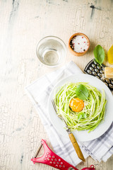 Trendy vegan food recipes, cheese zucchini spaghetti pasta with egg yolk with parmesan, olive oil and basil leaves, light concrete background copy space