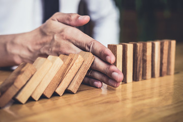 Strategy and successful intervention concept for business, businessman hand Stopping Falling wooden Dominoes effect from continuous toppled or risk - obrazy, fototapety, plakaty