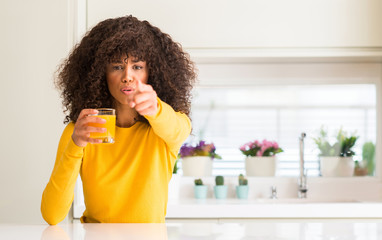 African american woman drinking orange juice in a glass pointing with finger to the camera and to...