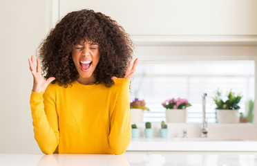 African american woman wearing yellow sweater at kitchen celebrating mad and crazy for success with...