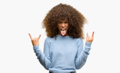 African american woman wearing a sweater shouting with crazy expression doing rock symbol with...