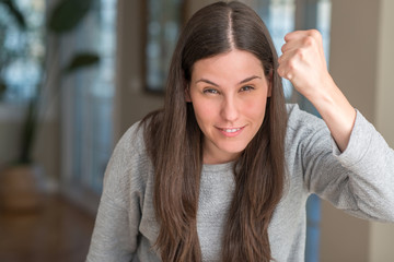 Young beautiful woman at home angry and mad raising fist frustrated and furious while shouting with anger. Rage and aggressive concept.