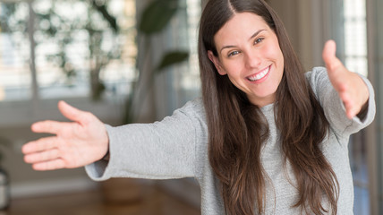 Young beautiful woman at home looking at the camera smiling with open arms for hug. Cheerful expression embracing happiness.