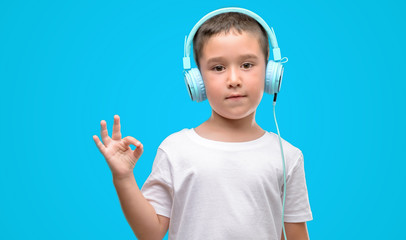 Dark haired little child listening music with headphones doing ok sign with fingers, excellent symbol