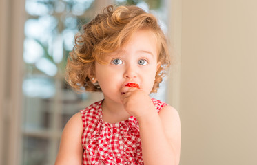 Beautiful blonde child with blue eyes eating strawberry at home.