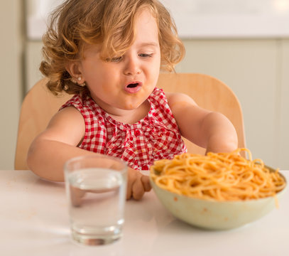 Beautiful blond child eating spaghetti with hands crying with tantrum at home.