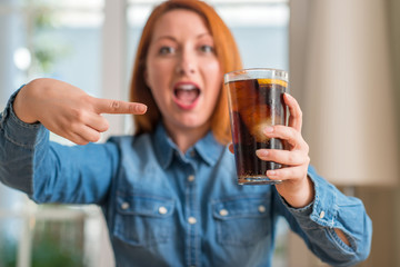 Redhead woman holding soda refreshment very happy pointing with hand and finger